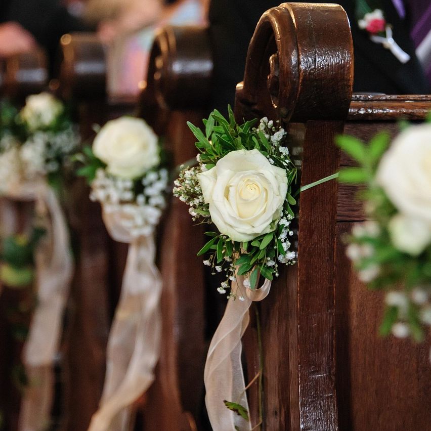 Nahaufnahme von Kirchenbänken, geschmückt mit weißen Rosen, grünen Blättern und zarten Schleifen – festliche Dekoration für eine Trauung