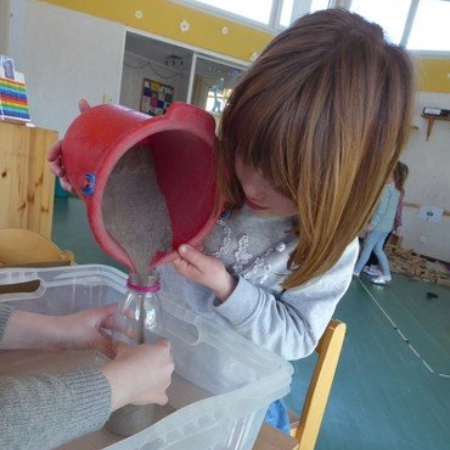 Kind füllt Sand in Flasche