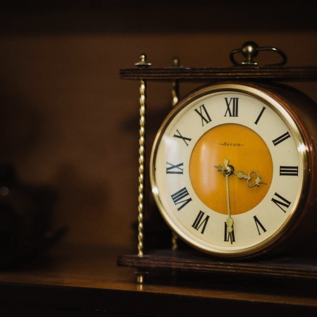 Gottesdiensttermine. Eine alte Uhr mit römischen Ziffern steht auf einer Vitrine